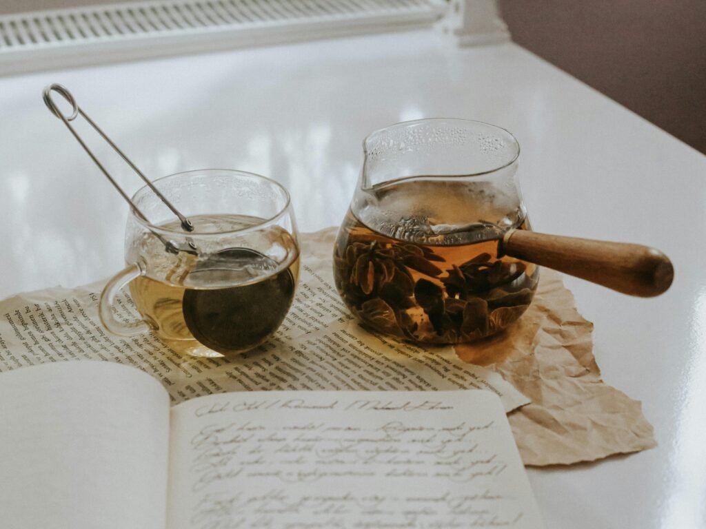 A warm tea scene with a glass cup, teapot, and open journal, evoking cozy indoor vibes.